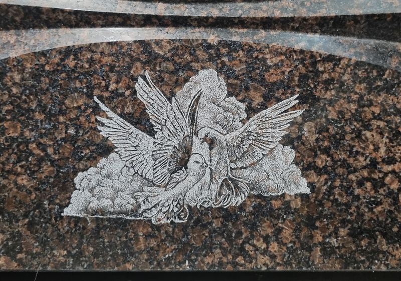 Коричнево-красный гранит с крупным зерном, гравировка пары голубей в облаках