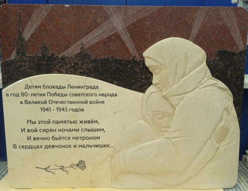 Горизонтальная мемориальная плита из красного гранита с объёмным светлым барельефом женщины с ребёнком, стоит в цехе